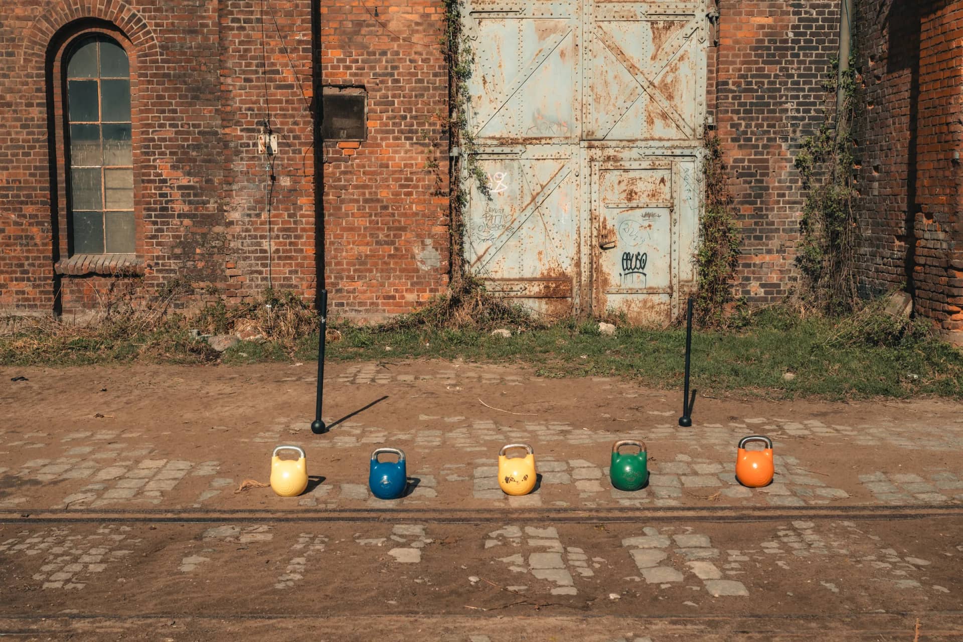 Incore Sports competition kettlebells and macebells lined up in front of an industrial brick building