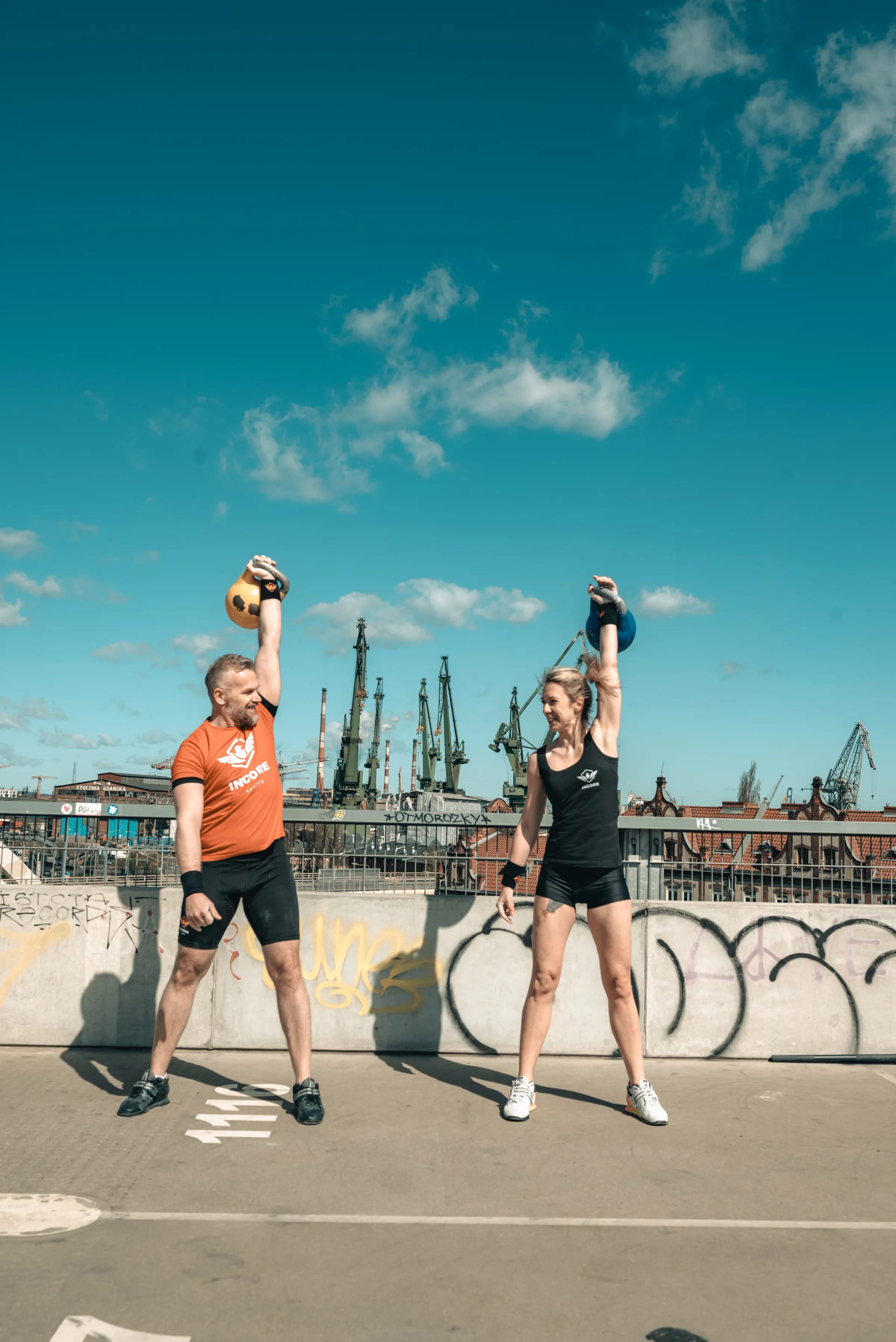 Dwójka zawodników Incore Sports wyciskających kettlebelle nad głową na dachu