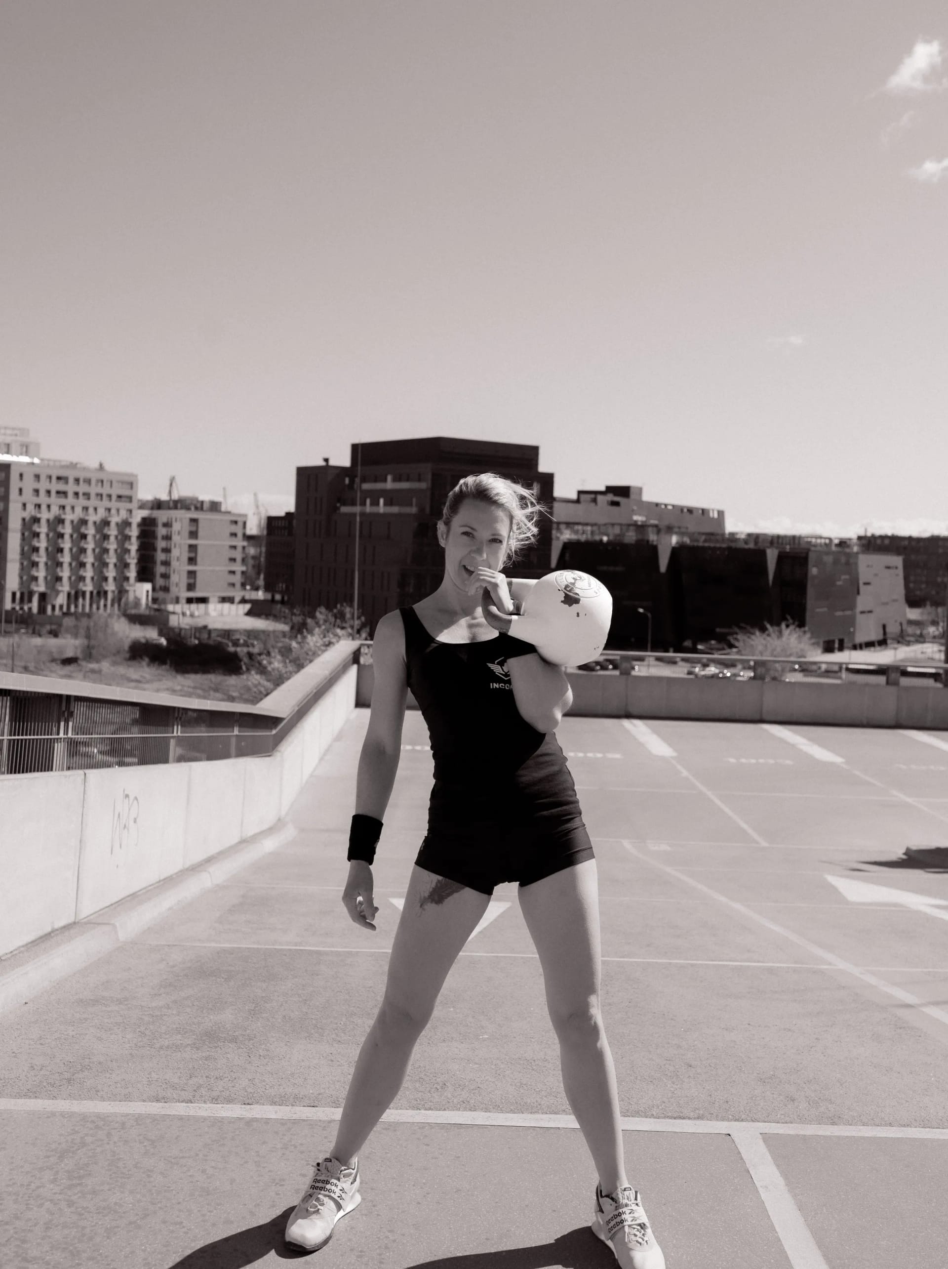 Athlete holding a white Incore Sports kettlebell on a rooftop, black and white