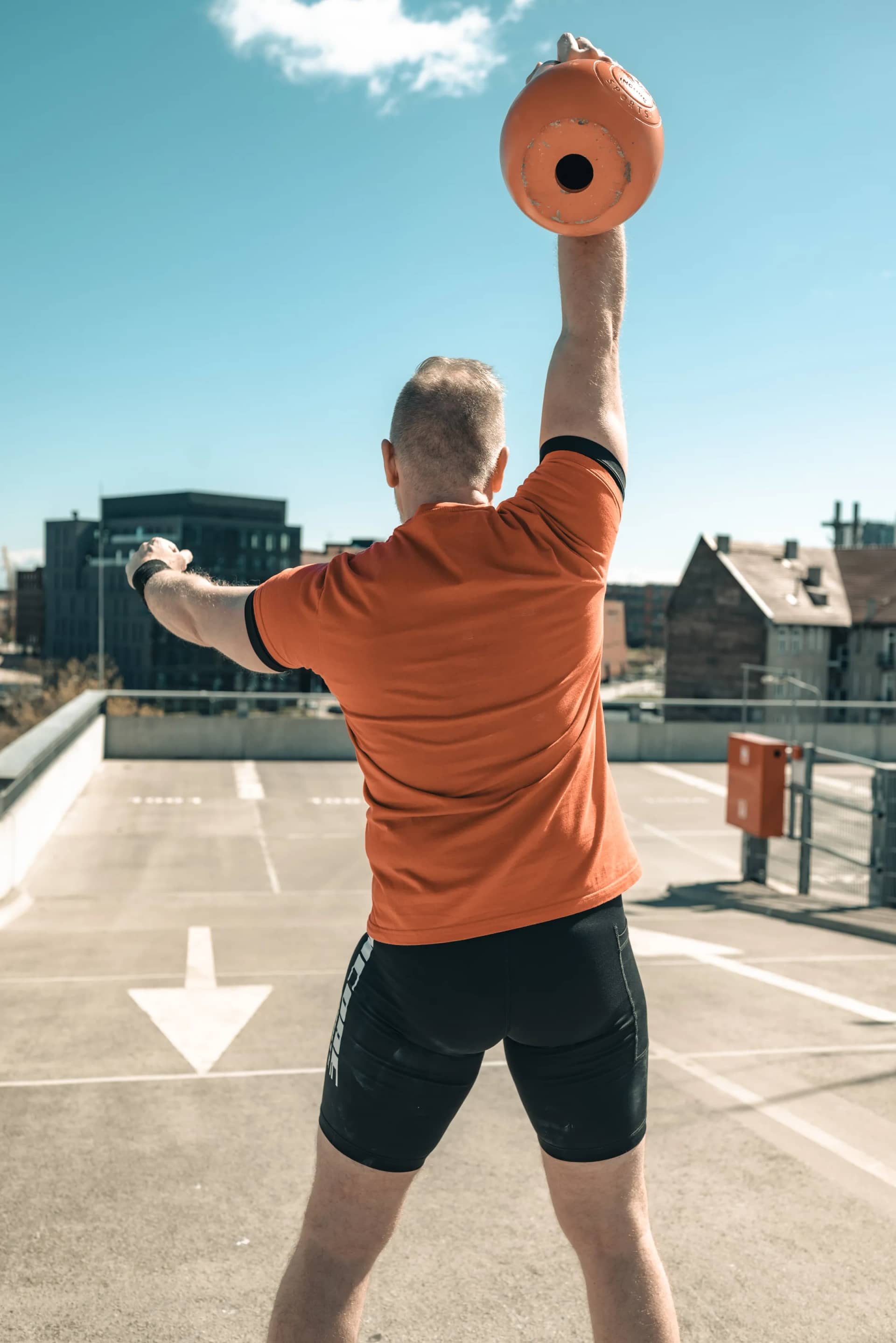 Athlete pressing an orange Incore Sports kettlebell overhead on a rooftop